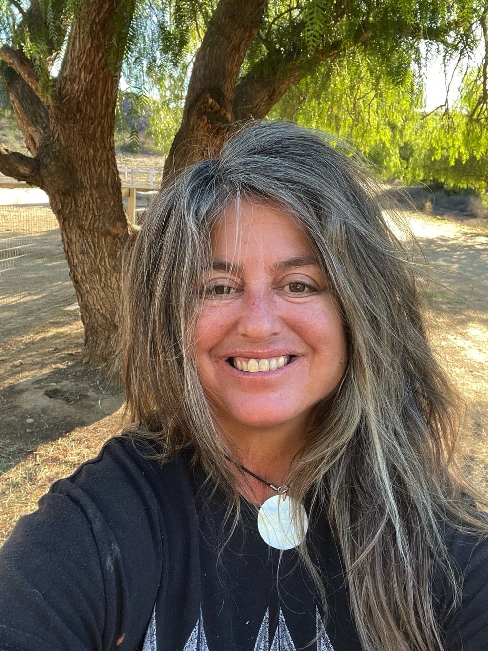 Portrait of Joy Baumann smiling outdoors beneath a tree